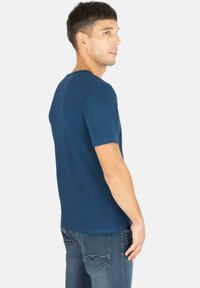 Marineblaue Kurzarm-T-Shirt mit rundem Ausschnitt, glattem Stoff und taillierter Passform, kombiniert mit blauen Jeans mit Gesäßtaschen.