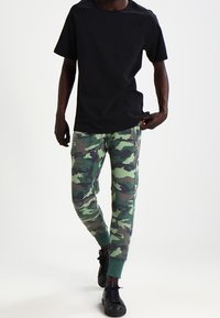 Svart t-shirt med kort ärm i kombination med gröna kamouflagemönstrade sweatpants med ribbade muddars. Svarta sneakers fulländar outfiten.