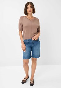 Top marrone a maniche corte e scollatura a V; pantaloni shorts in denim blu; scarpe piatte nere in rete. Outfit casual con una vestibilità comoda e un design semplice.