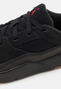 Sneakers noirs avec une tige en daim, des panneaux en maille et une semelle en caoutchouc noir. Des détails rouges sur l'emblème ajoutent un accent contrastant.