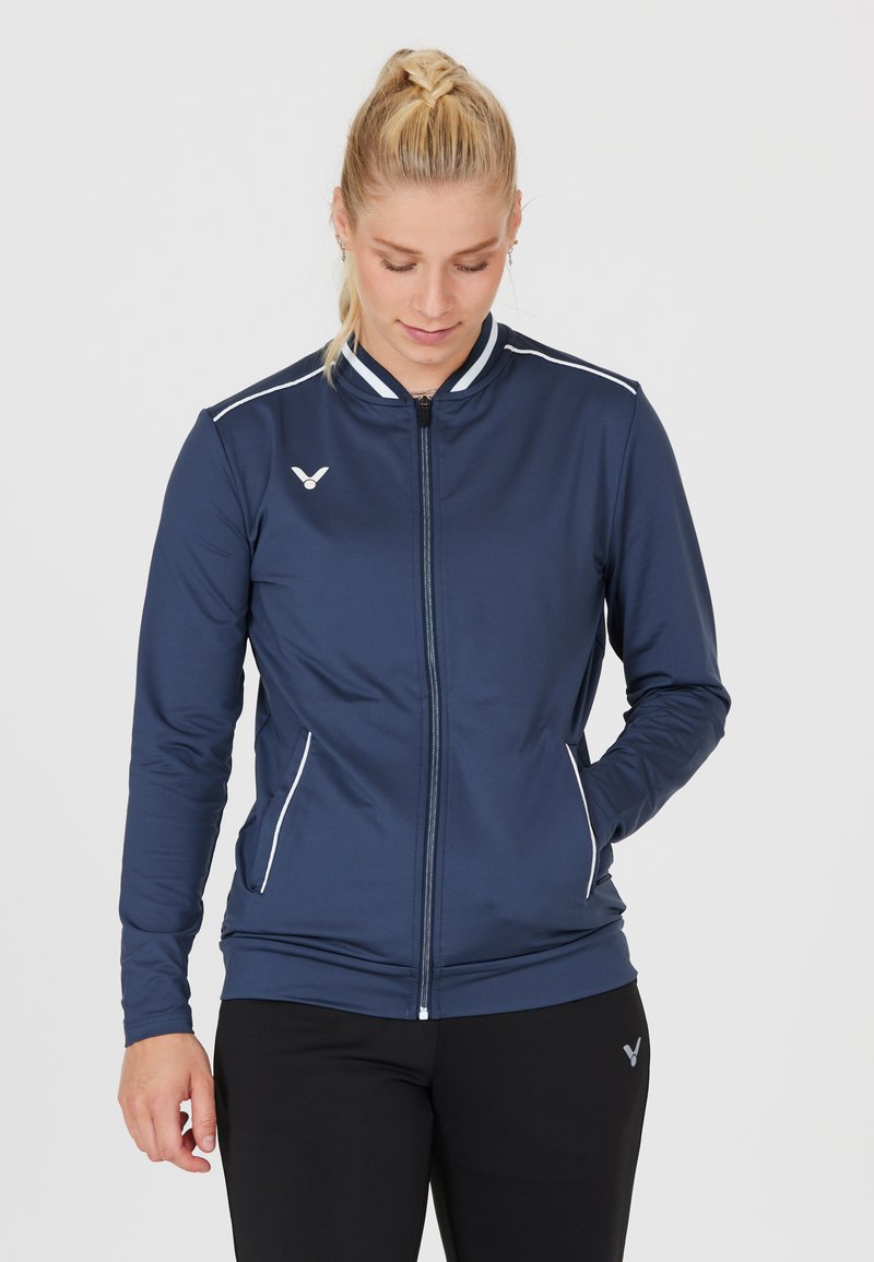 Havblå zip-up atletisk jakke lavet af glat stof, med hvide accenter og høj krave. Inkluderer sidelommer og et subtilt logo.