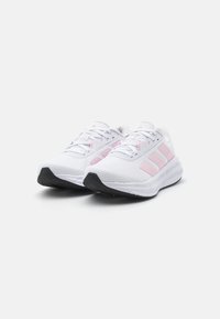 White athletic shoes with pink accents, mesh upper, lace-up closure, textured sole, and three stripes logo on the side.