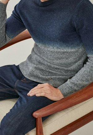 Sweter dziany z gradientem od ciemnoniebieskiego do jasnoszarego, z okrągłym dekoltem i ściągaczami na rękawach, zestawiony z ciemnoniebieskimi dżinsami.