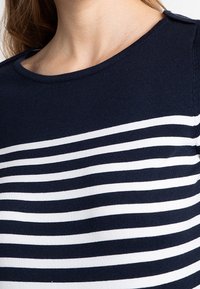 Suéter a rayas azul marino y blanco con cuello redondo, mangas cortas y detalle de botones en el hombro. Tejido de punto suave con textura lisa.