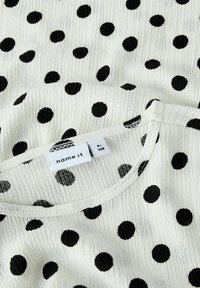 Witte stof met een gestructureerd oppervlak, voorzien van een algeheel patroon van grote zwarte polka dots. Ronde halslijn met een zichtbaar waslabel.