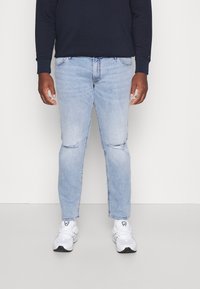 Ljusblå jeans med rivna detaljer, slim fit-design och lätt blekning. Kombinerat med vita sportskor och en marinblå långärmad tröja.