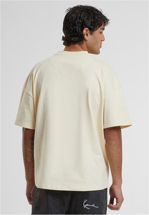 Cremefarvet oversized t-shirt med korte ærmer, glat tekstur, rund halsudskæring og et lille logo på bagsiden af kanten.
