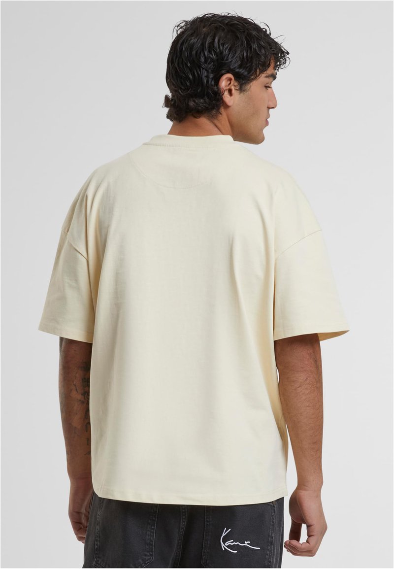 Kreminės spalvos per didelis marškinėlių su trumpomis rankovėmis, lygus paviršius, apvalus iškirpimas ir mažas logotipo detalė ant nugaros krašto.