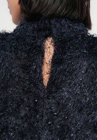 Tmavě modrý texturovaný oděv s chlupatým povrchem a výstřihem na zádech ve tvaru klíčové dírky. Tkanina má různorodá vlákna pro větší hloubku.