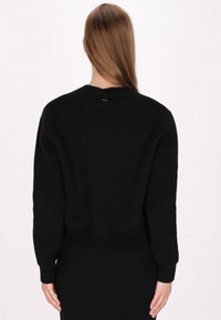 Schwarzer Strickpullover mit Rundhalsausschnitt, gerippten Bündchen und Saum. Glatte Textur und ein kleines metallisches Akzent auf der Rückseite.