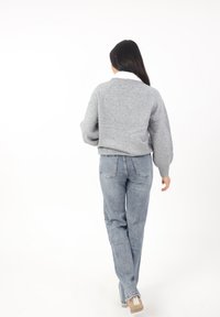 Grijze gebreide sweater met een ronde halslijn en ballonmouwen, gecombineerd met lichtblauwe rechte jeans. Achteraanzicht, gladde textuur.