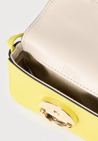 Gul læderhåndtaske med en lukning i guldhardware, med en glat yderside og en beige indvendig foring. "Furla" præget på foringen.
