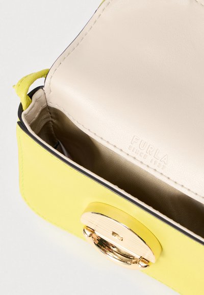 Sac à main en cuir jaune avec une fermeture à clapet en métal doré, présentant un extérieur lisse et une doublure intérieure beige. "Furla" embossé sur la doublure.