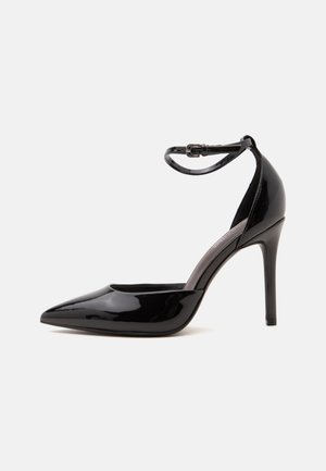 Chaussure noire à talon haut avec bout pointu et finition brillante, équipée d'une bride autour de la cheville avec une petite boucle.