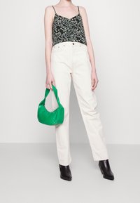 Un crop top noir à fleurs avec des bretelles fines, un jean droit couleur crème, et un sac à main vert. Des bottes à talons noires complètent la tenue.