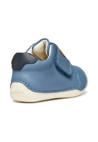 Scarpa in pelle blu con una striscia in velcro, fodera beige, suola in gomma e cuciture a contrasto. Il retro presenta un piccolo logo bianco.