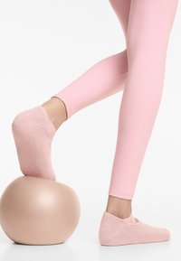 Ljust rosa platta strumpor med ribbad textur, i kombination med matchande rosa leggings, vilande på en matt beige träningsboll.