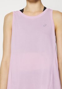 Vaaleanpunainen urheilutoppi, joka on valmistettu sileästä ja hengittävästä materiaalista. Topissa on pyöreä pääntie ja hienovarainen logo edessä.