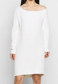 Robe blanche en tricot à épaules dénudées avec manches longues, texture côtelée et coupe décontractée, dotée d'un ourlet droit et de détails subtils.