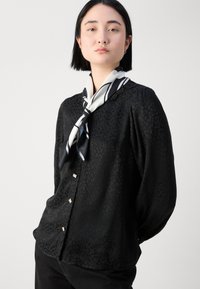 Blouse noire à manches longues avec un motif animal léger, en tissu léger, boutons décoratifs et un foulard en soie à motifs blancs et noirs.