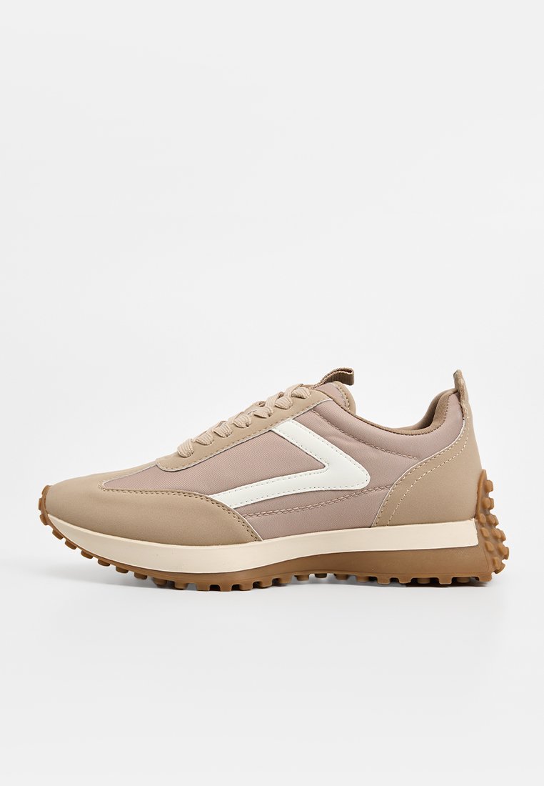 Zapatillas deportivas beige con tejido texturizado, detalles en blanco, punta redonda, diseño de cordones y suela de goma estriada para tracción.