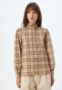 Bruin en beige geruite lang-sleeve shirt met een hoge kraag, opstaande schouders en knoopsluiting, gemaakt van zachte stof met een subtiele textuur.