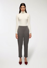 Biała rypsowa bluzka z golfem, szare dopasowane spodnie i czerwone buty na szpilkach. Strój charakteryzuje się dopasowanym krojem i czystymi liniami.