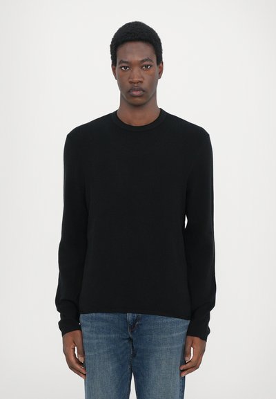 Sort ribbet langærmet sweater med rund hals, parret med lyseblå jeans. Glat tekstur, tætsiddende silhuet, minimalistisk design.