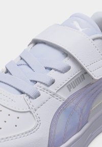 Λευκό αθλητικό παπούτσι Puma με φωτεινή μωβ ιριδίζουσα λωρίδα, λουράκι με βέλκρο και κορδόνια που διασταυρώνονται, πάνω σε λευκό φόντο.