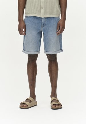 Denim shorts i lyseblå farve med oprullede ben, klassisk skæring. Kombineret med beige sandaler. Struktureret strik cardigan i beige.