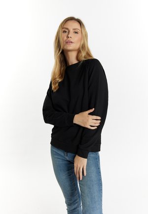 Felpa nera con collo rotondo, maniche lunghe e polsini a costine. Indossata con jeans blu, presenta una superficie liscia e una vestibilità comoda.