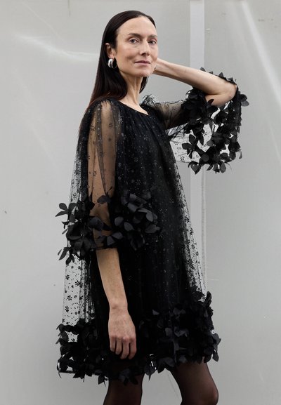 Schwarzes transparentes Kleid mit Blumenmustern, voluminösen Ärmeln, die mit schwarzen Stoffblumen verziert sind, und einer lockeren, fließenden Silhouette.