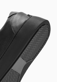 Sneaker en cuir noir avec un design élégant, tige texturée et semelle en caoutchouc avec un motif chevron. Bordure d'accent en gris mat.