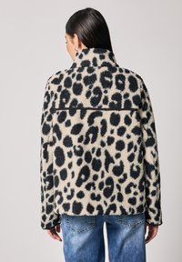 Chaqueta de forro polar con estampado de leopardo en beige con manchas negras, con cuello alto y corte relajado, combinada con jeans de mezclilla azul.