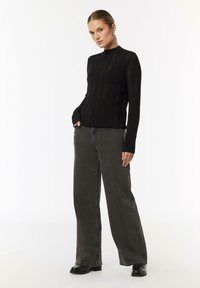 Schwarzes langärmliges Strickoberteil mit gerippter Textur und Stehkragen, kombiniert mit grauen weit geschnittenen Jeans und schwarzen Stiefeletten.