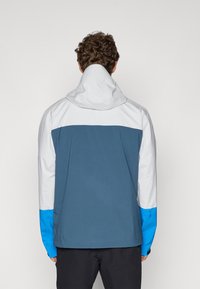Veste de plein air pour homme au design en coloris blocs avec un corps gris, une partie supérieure blanche et des accents de manches bleues. Le matériau semble lisse et léger.