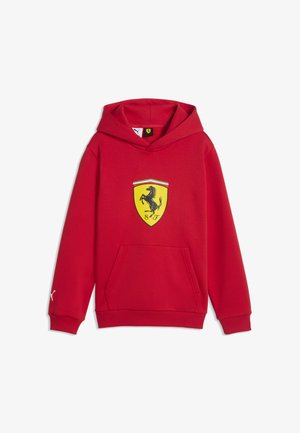 Czerwona bluza z kapturem z przednią kieszenią oraz żółtym logo Ferrari w kształcie tarczy z czarnym koniem w galopie i pasami w kolorach włoskiej flagi.