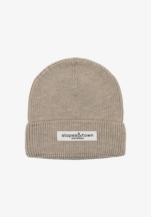 Beige gestrickte Mütze mit Umschlag, ausgestattet mit einem weißen Etikett mit schwarzer Schrift. Die Textur ist weich und verfügt über ein geripptes Design.