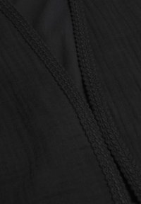 Gros plan sur un tissu noir montrant une couture diagonale avec une couture tressée décorative et texturée le long du bord.
