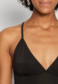 Černý halter top s tenkými ramínky, vybavený výstřihem ve tvaru V a nařasenými detaily. Hebký povrch, minimalistický design.