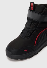 Zwarte winterlaars met een gepadded ontwerp, zwarte en rode accenten, elastische veters en een gestructureerde rubberen zool met het Puma-logo.