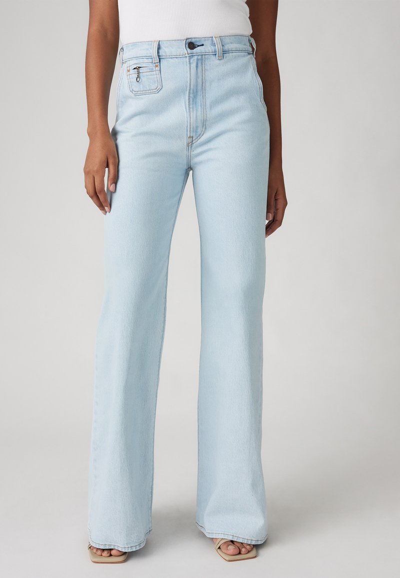 Jean flare taille haute bleu clair en denim, avec une poche avant dotée d'un détail zippé et une couture subtile sur les coutures.