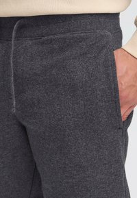 Pantalons de survêtement gris en tissu doux et texturé, avec une taille côtelée, un cordon de serrage élastique et des poches latérales.