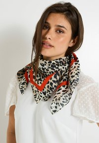 Bufanda de seda con estampado de leopardo que presenta un borde geométrico rojo; forma triangular; tejido ligero con una textura suave. Llevada alrededor del cuello.