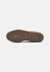 Shoe sole features a brown rubber base with circular grip patterns and defined treads; gray accents near the heel and logo detail present.