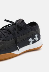 Scarpa sportiva nera con una parte superiore testurizzata, dotata di un logo bianco, chiusura con lacci e suola in gomma.