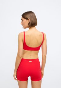 Κόκκινο αθλητικό σουτιέν και σετ σορτς με ψηλή μέση. Λείος ύφασμα, μινιμαλιστικός σχεδιασμός, χωρίς σχέδια, με μικρό λογότυπο στη μέση.