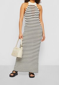 Robe maxi tricot à col halter rayée en crème et noir, associée à un sac seau crème et des sandales noires. Tissu texturé et design ajusté.