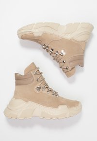 Zapatillas altas de ante beige con suelas de goma gruesas en color crema, herrajes plateados en los cordones y detalles de costura de acento.