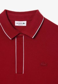 Röd polo t-shirt med en texturerad tyg, vit krage och en liten broderad logotyp på vänster bröst. Design med regular fit.